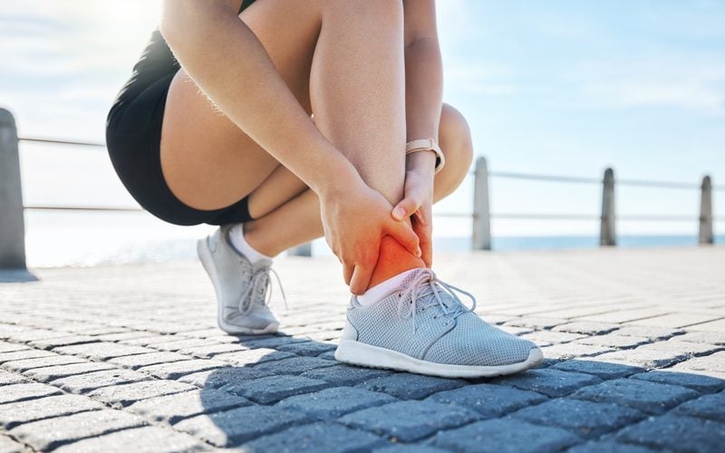 Woman running outdoors stopping to hold her painful ankle before chiropractic treatment in Centennial CO