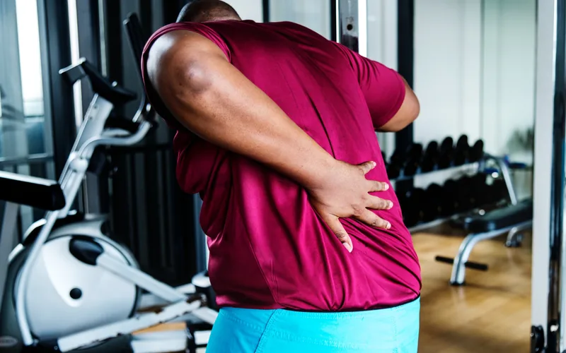 Man at the gym holding his back from pinched nerve pain in Centennial CO