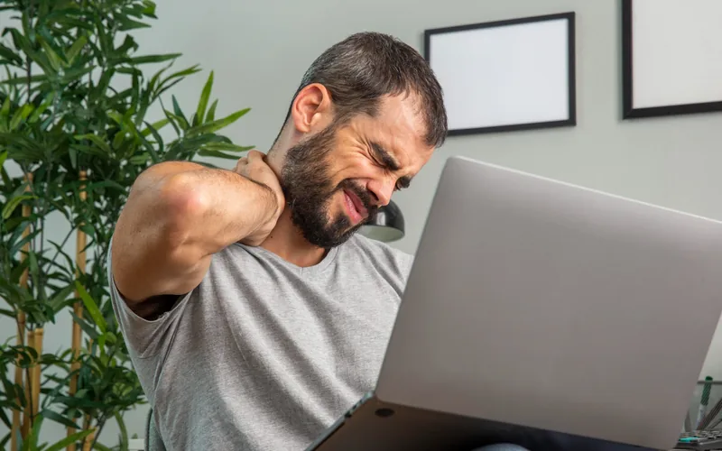 Man at his laptop holding his neck from desk posture neck pain in Centennial CO