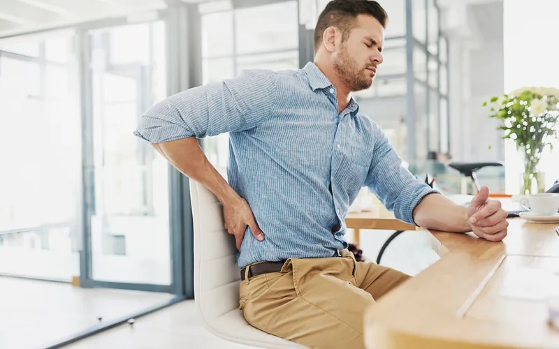 Office worker holding his lower back in pain, treated at Axis Health and Wellness in Centennial CO